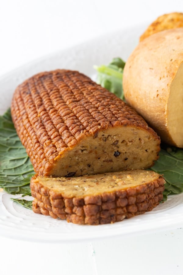 A Field Roast Celebration Roast with a slice cut from the end on a white platter on a green leaf