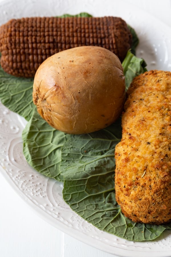 Three vegan turkey roasts on a white platter on greens,.