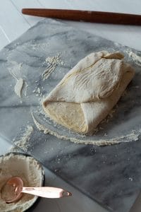 croissant dough being folded into an envelope on a marble board on the third fold