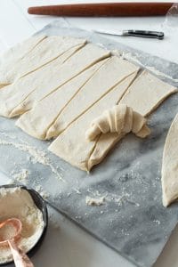 vegan croissant dough being rolled into a crescent shape on marble