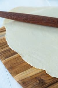 Pasta dough rolled out thin on a wood board with a wooden rolling pin