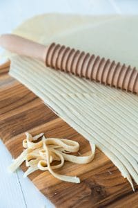 A wooden pasta cutting roller making noodles out of pasta dough