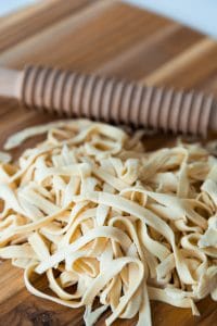 Homemade pasta noodles on a wood board with a pasta cutting roller next to the noodles