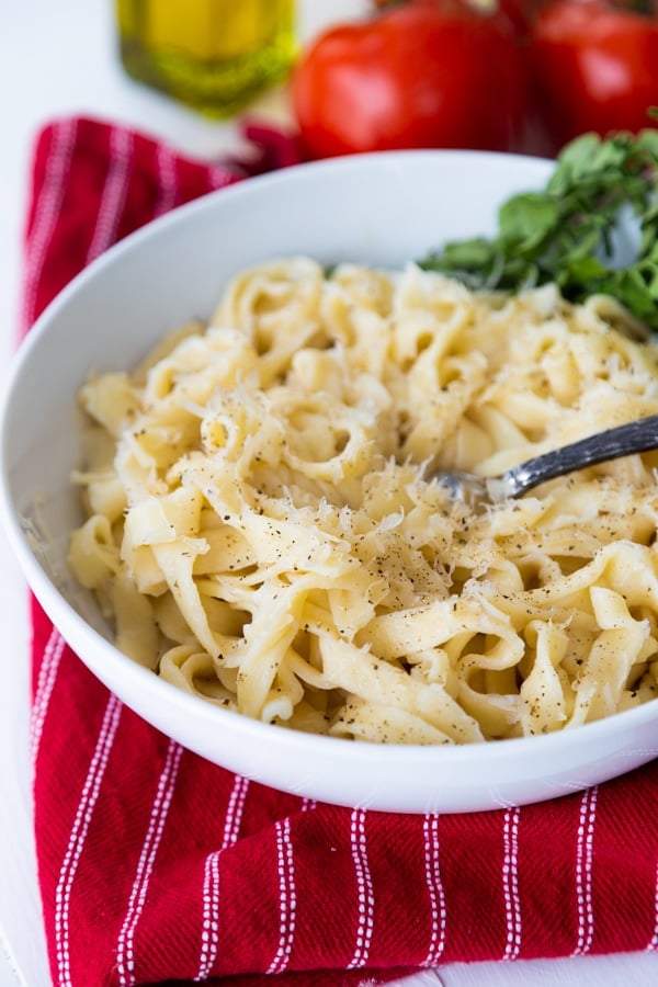 Homemade vegan pasta in a white bowl with a fork in the center on a red towel with herbs on the side of the bowl.