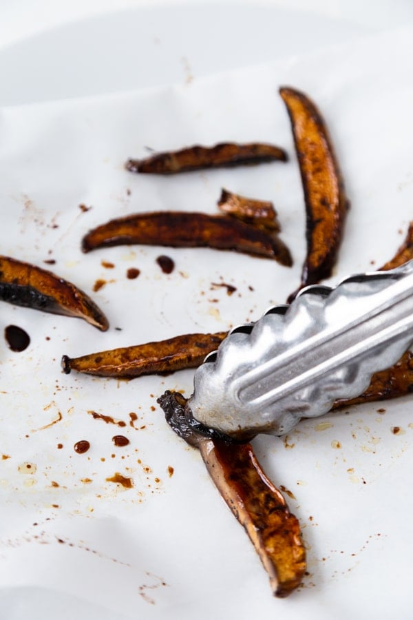 Strips of mushroom bacon on parchment papper with a silver tong placing a piece of bacon on the paper