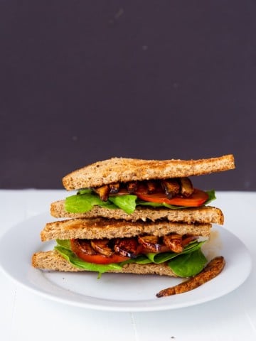 A PLT sandwich cut in half and stacked on a white plate