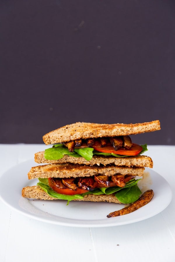 A PLT sandwich cut in half and stacked on a white plate