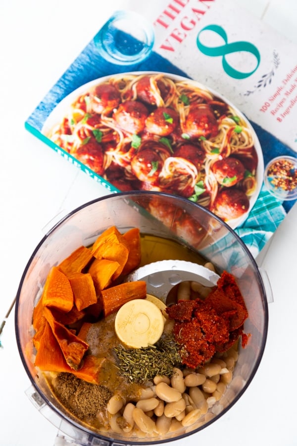 The ingredients for a curry dip in a food processor with The Vegan 8 cookbook next to it.