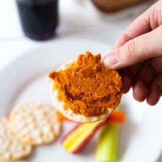 Curry dip on a cracker with a white plate with extra crackers and sliced vegetables.