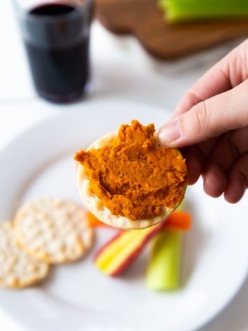 Curry dip on a cracker with a white plate with extra crackers and sliced vegetables.