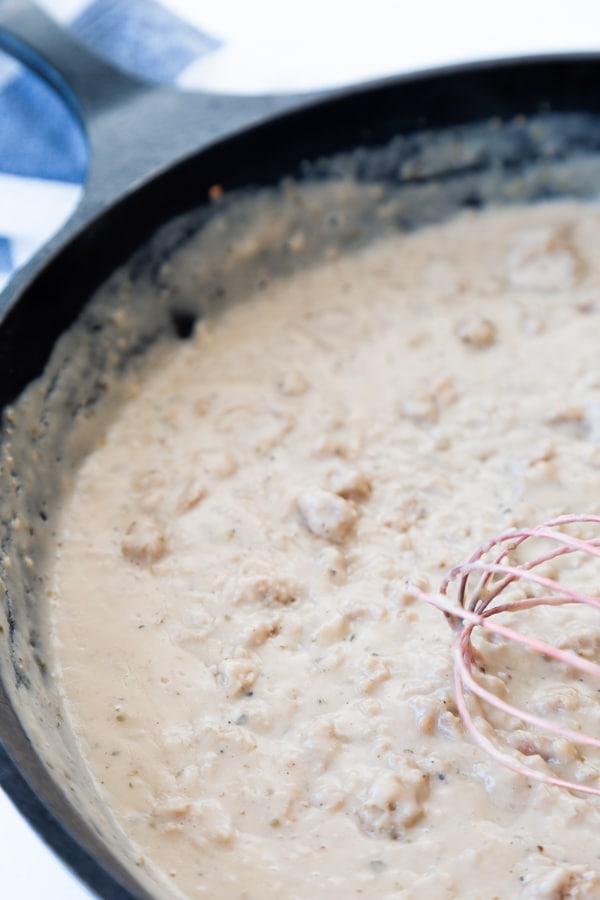 Sausage gravy being whisked in an iron skillet