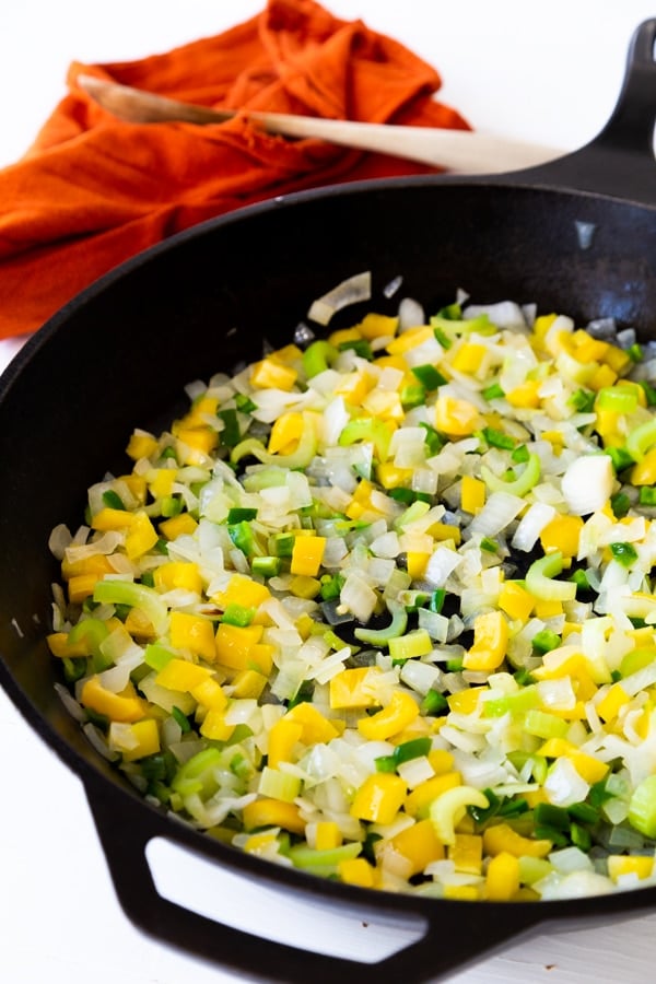 Onions, celery, and peppers cooking in a cast-iron skillet 