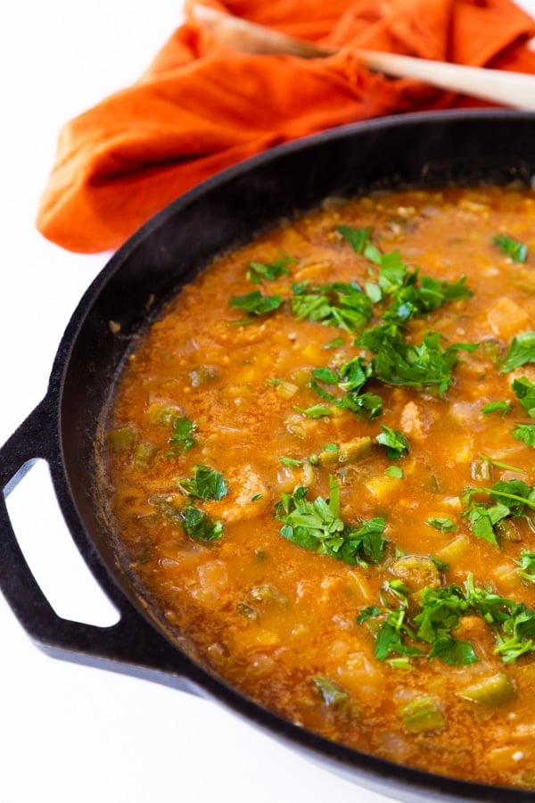 Gumbo being cooked in a cast-iron skillet with chopped parsley sprinkled on top.