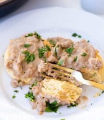 Biscuits and gravy on a white plate with a gold fork