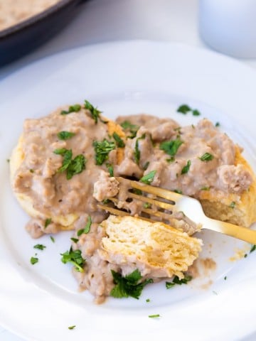 Biscuits and gravy on a white plate with a gold fork