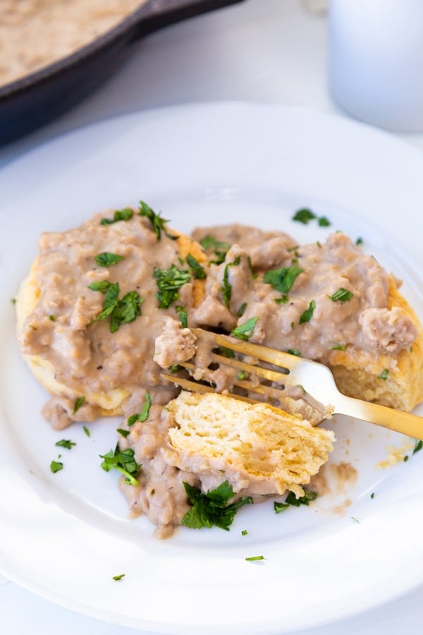 Biscuits and gravy on a white plate with a gold fork 