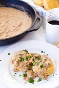 Biscuits and gravy on a white plate with a cup of coffee and a skillet of gravy in the background featured on Veganosity