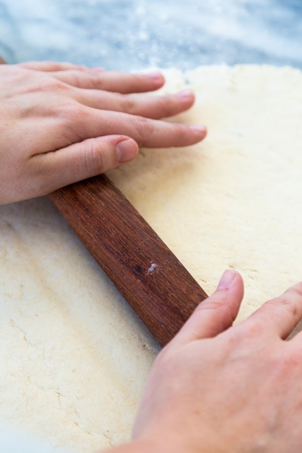 Hands rolling out dough with a wood rolling pin