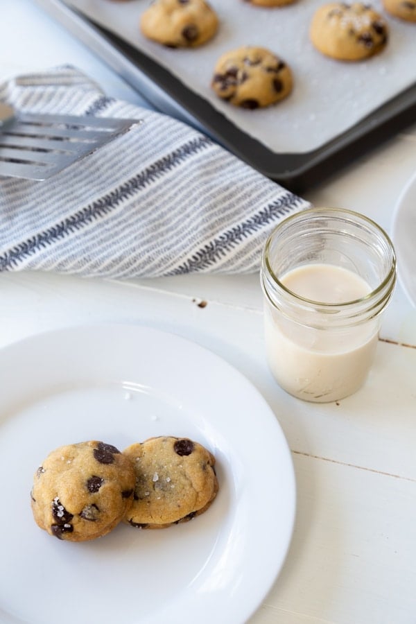 A plate of chocolate chip cookies and a baking sheet with more cookies in the background.