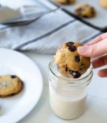 A hand dunking a chocolate chip cookie in a glass of milk