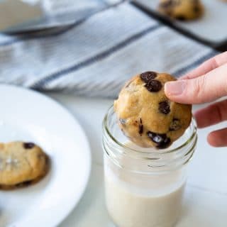 A hand dunking a chocolate chip cookie in a glass of milk