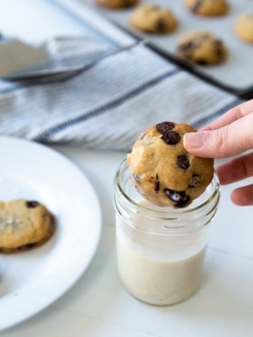 A hand dunking a chocolate chip cookie in a glass of milk