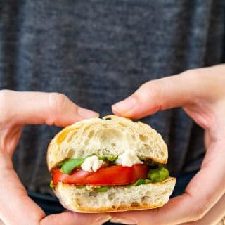 Two hands holding a caprese salad sandwich.