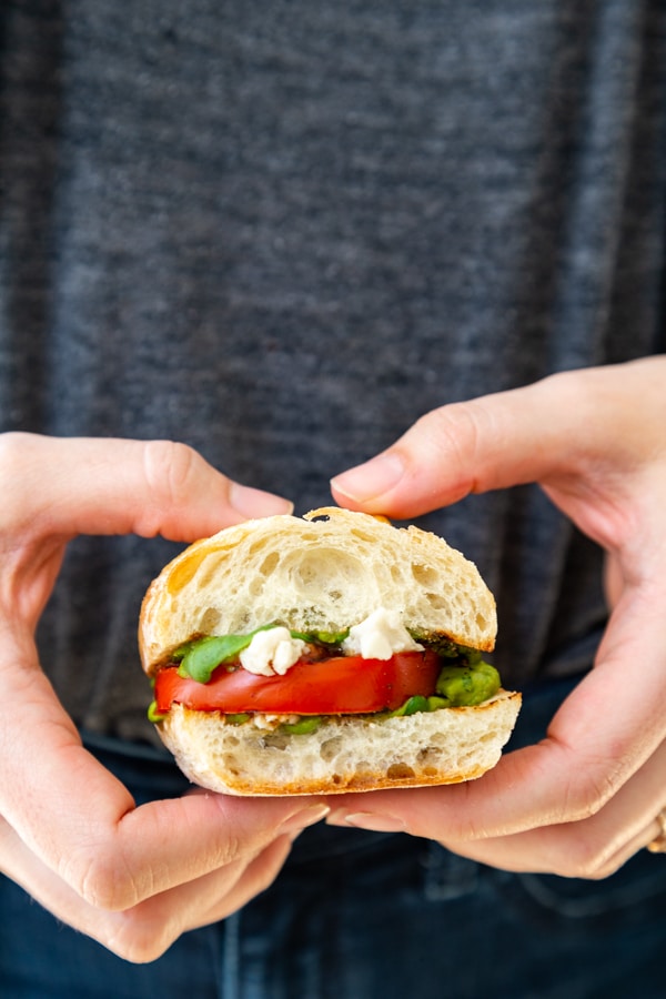 Two hands holding a caprese salad sandwich. 