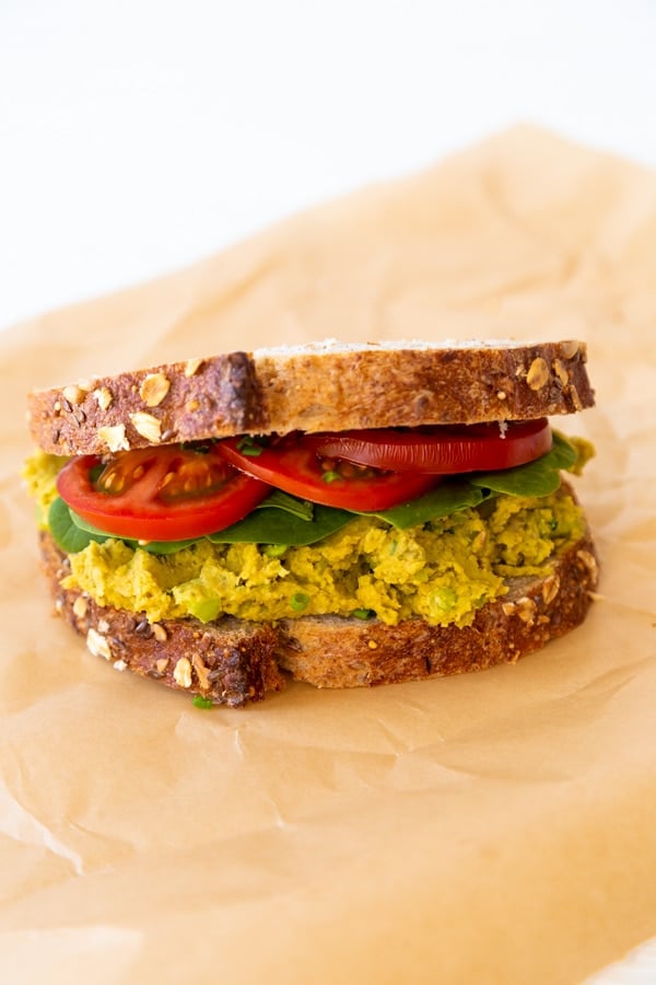 A smashed chickpea, spinach, and tomato sandwich on parchment paper.