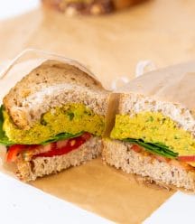 A smashed chicikpea salad sandwich cut in half and wrapped in parchment paper