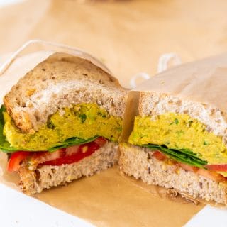 A smashed chicikpea salad sandwich cut in half and wrapped in parchment paper