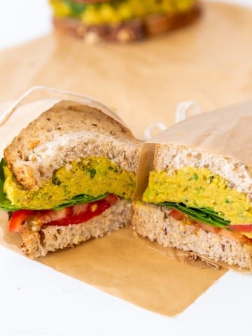 A smashed chicikpea salad sandwich cut in half and wrapped in parchment paper