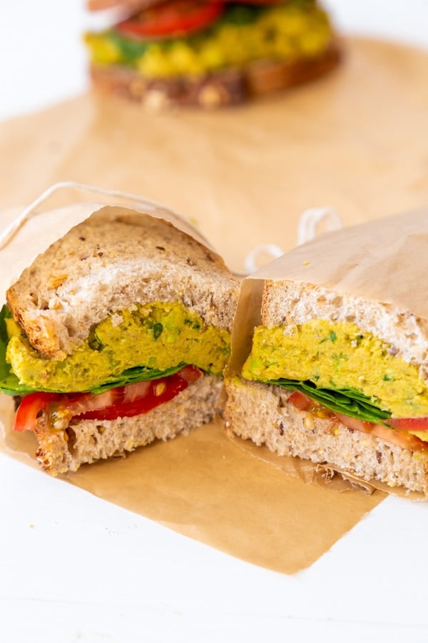 A smashed chicikpea salad sandwich cut in half and wrapped in parchment paper