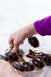 chocolate Easter eggs in a candy mold with a woman's hand touching an egg.