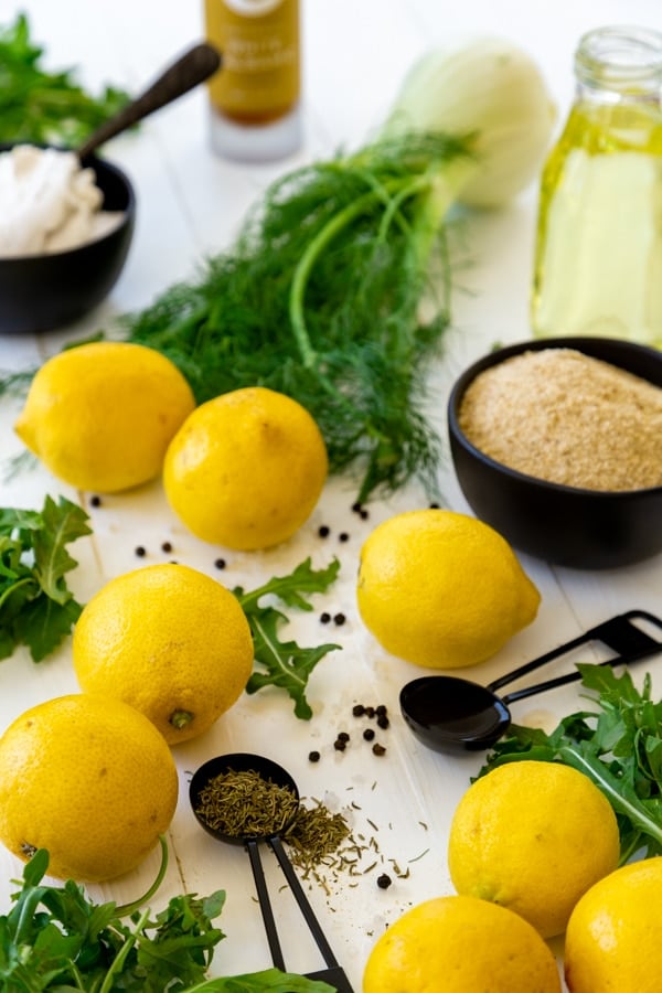 Ingredients for arugula and fennel salad with fried lemons including lemons, fennel, and spices in black measuring cups and spoons on a white board.