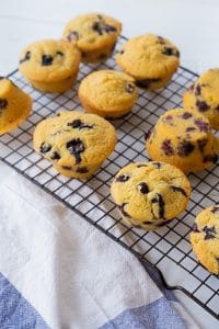 Blueberry muffins cooling on a wire rack with a white and blue towel next to them.