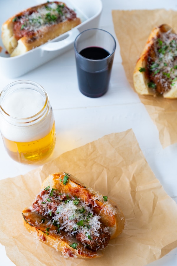 3 of our vegan meatball sub on parchment paper with a beer and a glass of wine next to them. 