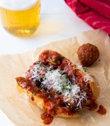 A meatball sub created by Veganosity on parchment paper with a beer in the background
