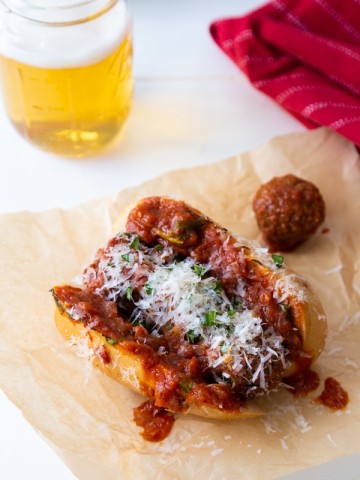 A meatball sub created by Veganosity on parchment paper with a beer in the background