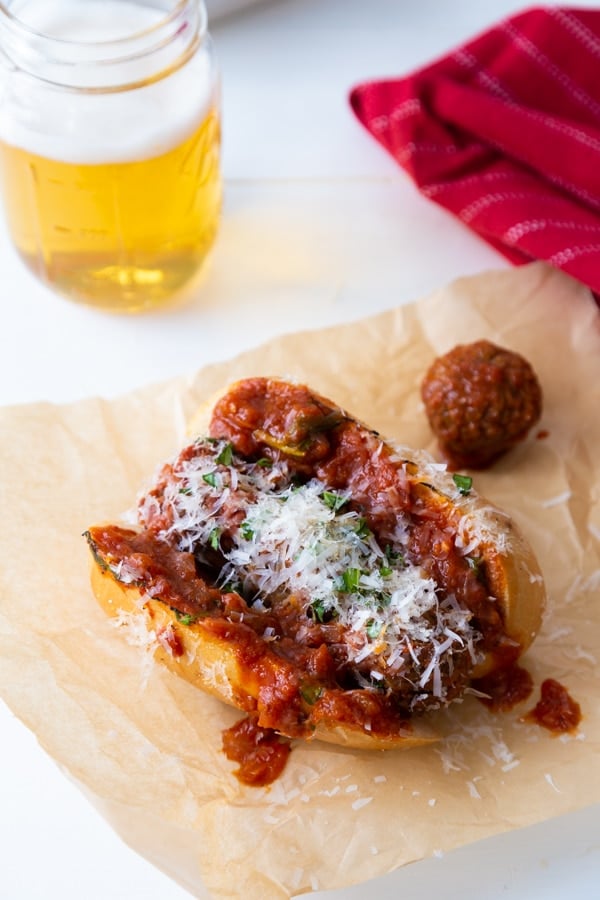 A vegan meatball sub on parchment paper with a beer in the background