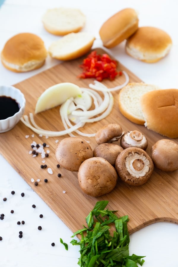 A cutting board with mushrooms, onion, and hamburger buns