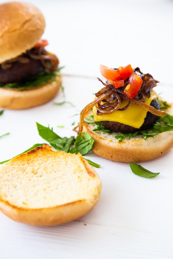 An open face mushroom slider with melted cheese, fried onions, shredded greens and chopped tomatoes