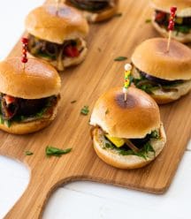 Mushroom sliders on a wood board with toothpicks in the center of the buns.