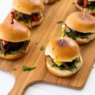 Mushroom sliders on a wood board with toothpicks in the center of the buns.