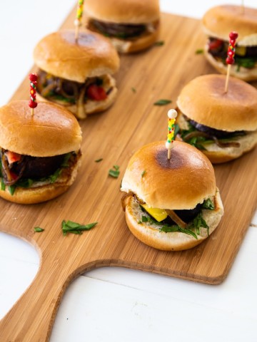 Mushroom sliders on a wood board with toothpicks in the center of the buns.