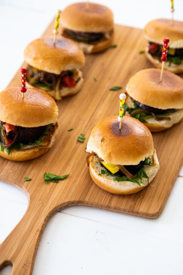 Mushroom sliders on a wood board with toothpicks in the center of the buns. 