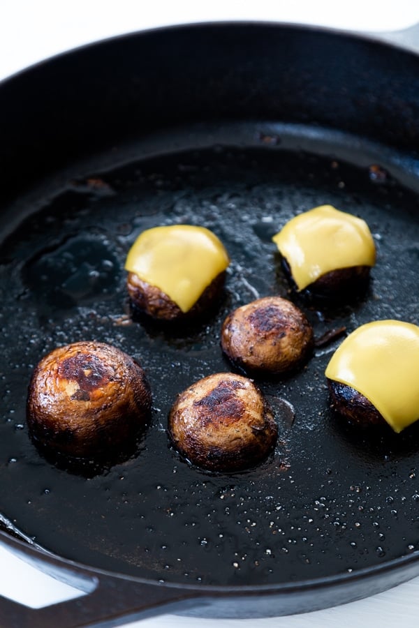 Mushroom caps and some with cheese on top in an iron skillet