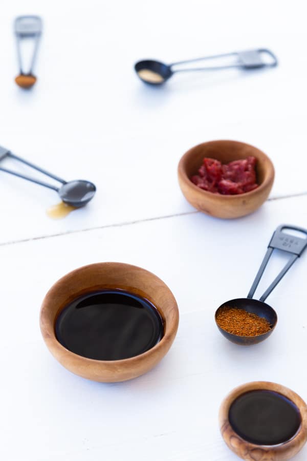 Wooden bowls and black measuring spoons with spices and liquids