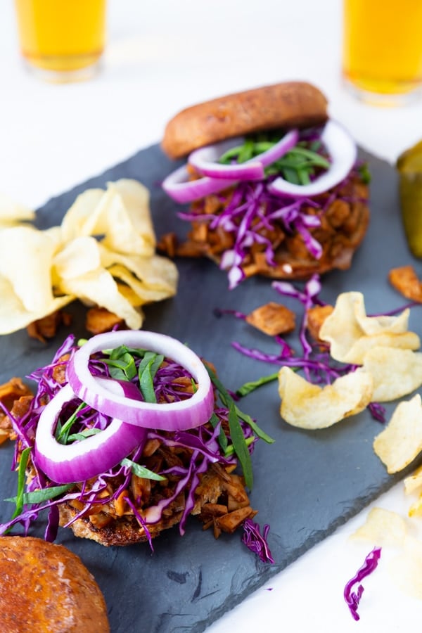 Two BBQ sandwiches with potato chips and two glasses of beer.