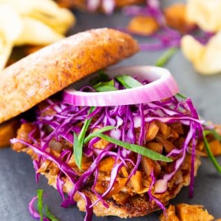 A pulled BBQ sandwich featured in the Veganosity cookbook Great Vegan BBQ Without a Grill with the bun half on the top and onions and slaw on top of the sandwich